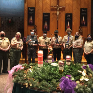 Scouts with lanterns lit by Peace Light, behind Advent wreath